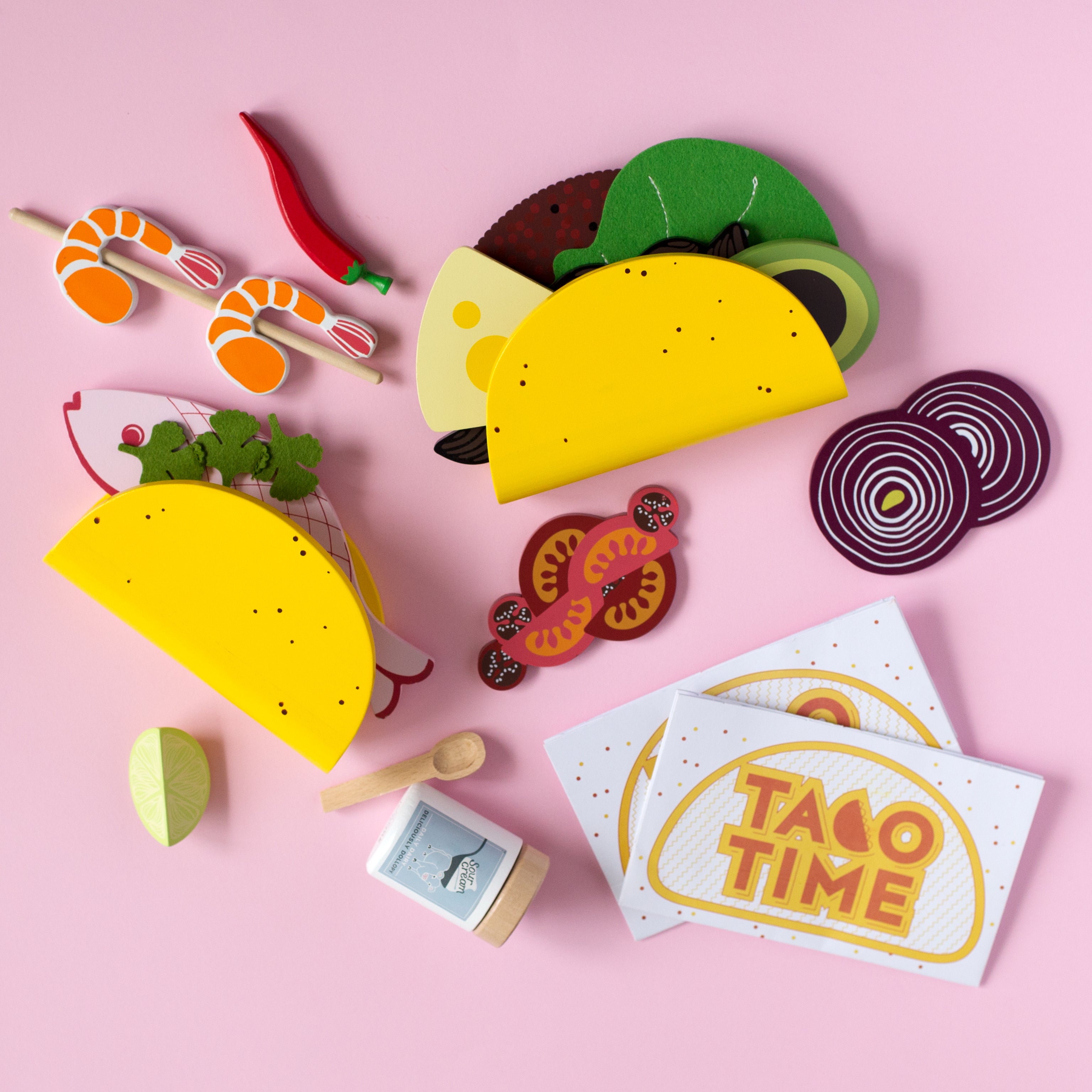 Make Me Iconic 21-piece wooden toy play Taco Kit featuring stand-up taco shells, prawns on skewers, paper takeaway bags, felt toppings, and pretend condiments like chilli sauce and sour cream for imaginative role play.