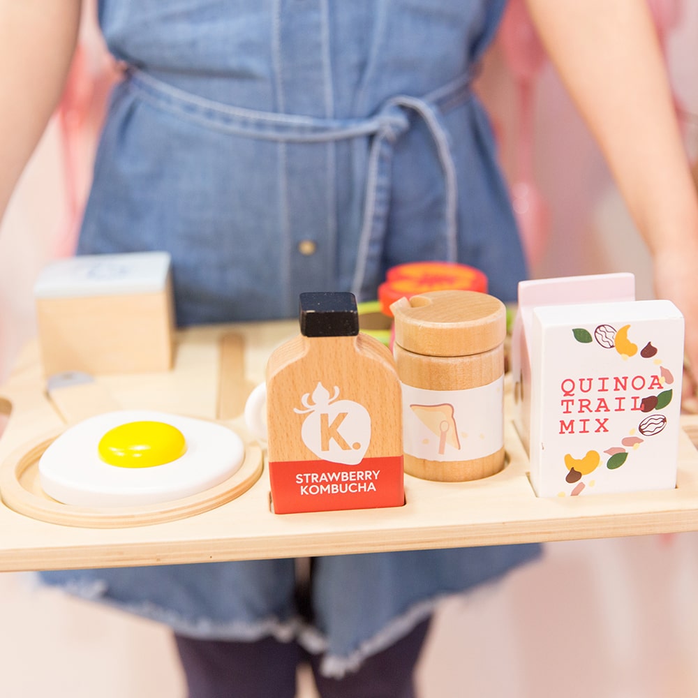 21-piece wooden toy breakfast tray featuring avocado on toast, goats cheese, tahini, kombucha, and other café-style foods for pretend play fun.