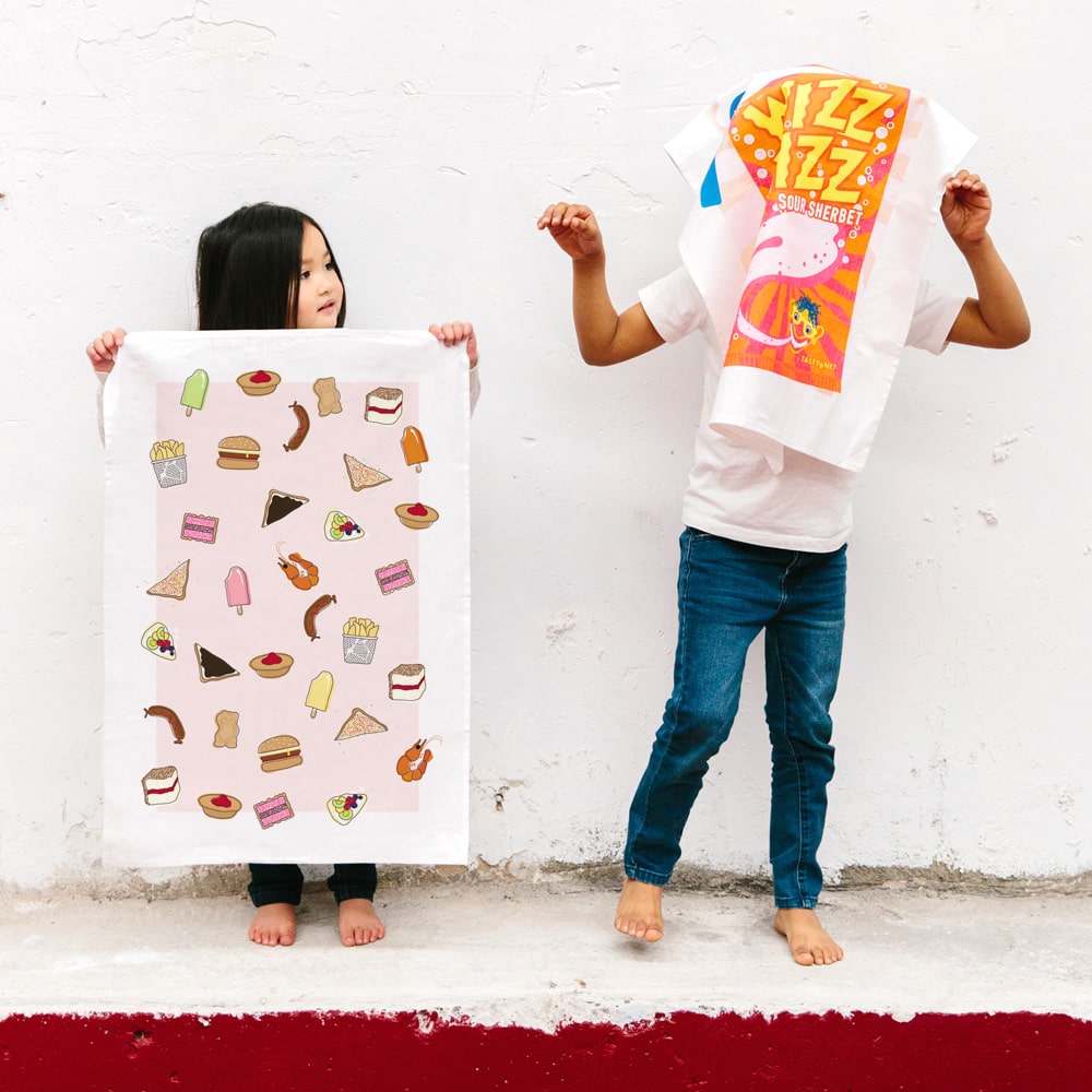 Make Me Iconic tea towel featuring iconic Australian foods, such as Vegemite toast, fairy bread, meat pies, pavlova, and lamingtons. A colourful, quirky kitchen accessory celebrating Aussie culture and nostalgia