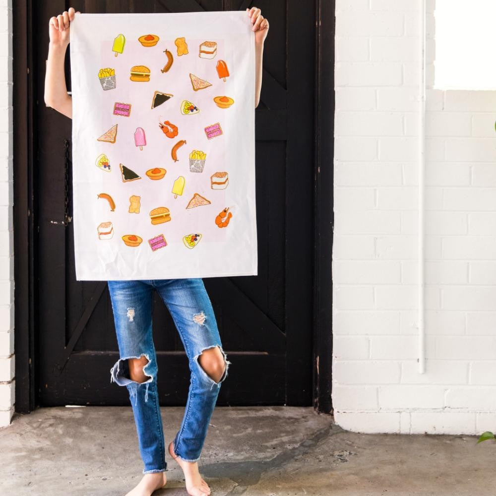 Make Me Iconic tea towel featuring iconic Australian foods, such as Vegemite toast, fairy bread, meat pies, pavlova, and lamingtons. A colourful, quirky kitchen accessory celebrating Aussie culture and nostalgia