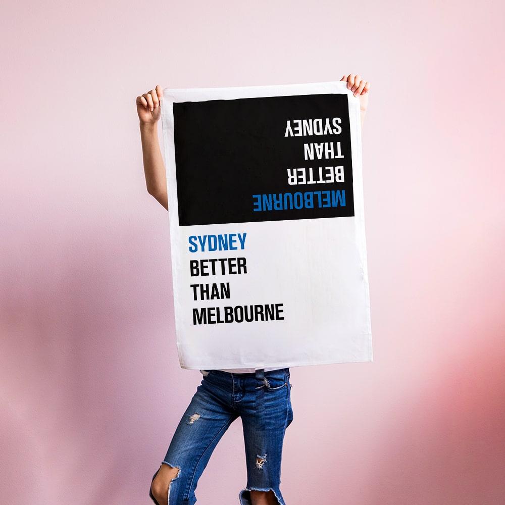 Make Me Iconic Choice Tea Towel with bold double-sided print, Melbourne vs Sydney rivalry in playful, nostalgic kitchen style.