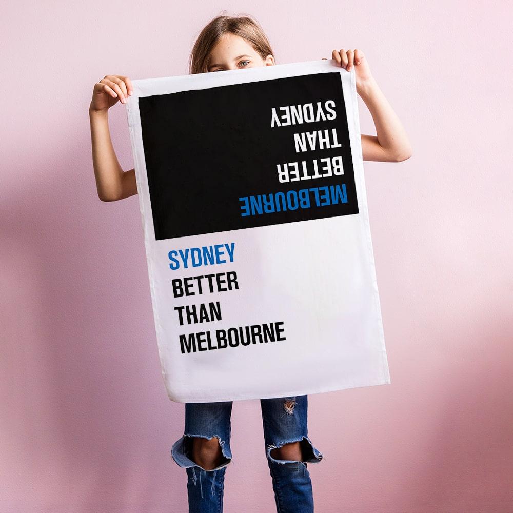 Make Me Iconic Choice Tea Towel with bold double-sided print, Melbourne vs Sydney rivalry in playful, nostalgic kitchen style.