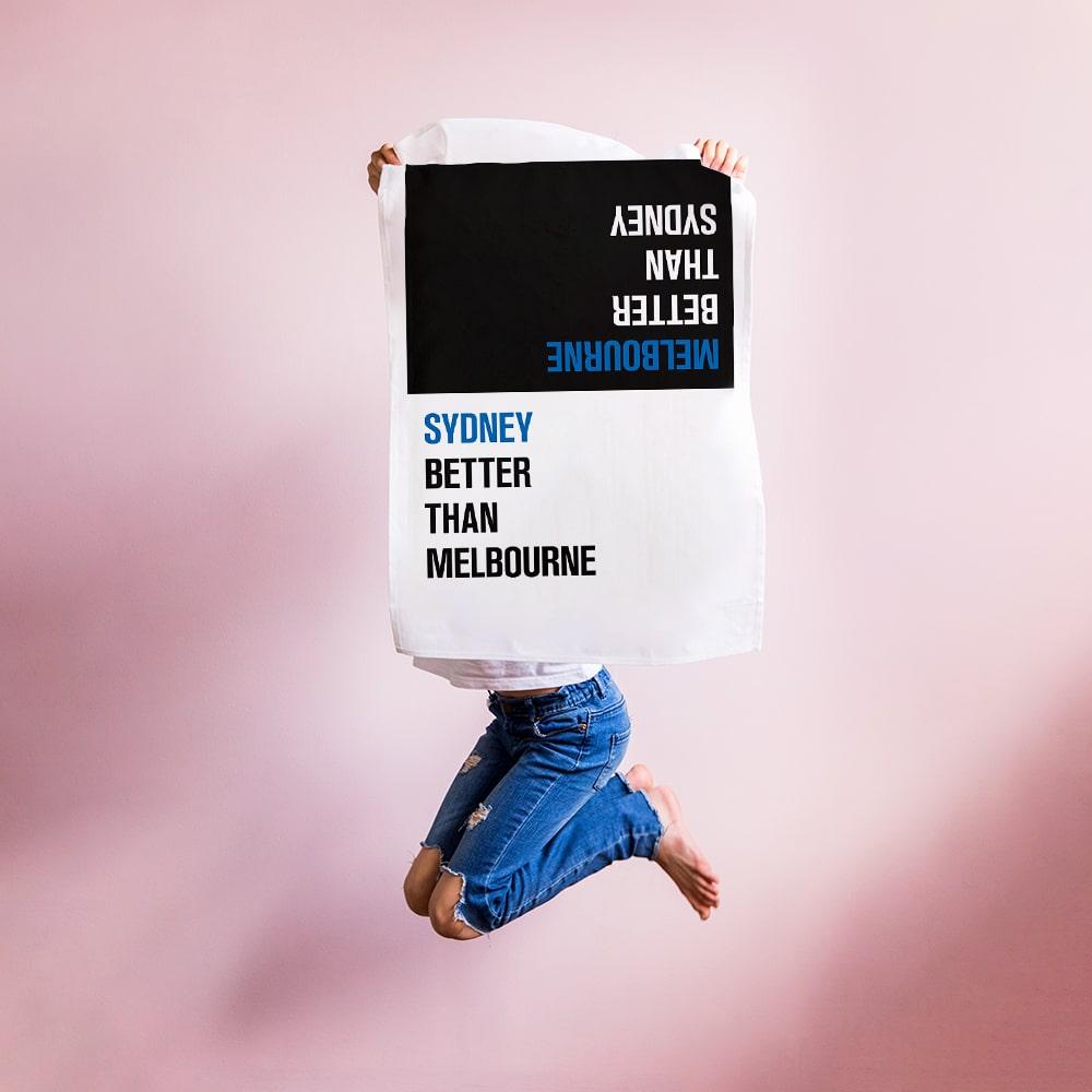 Make Me Iconic Choice Tea Towel with bold double-sided print, Melbourne vs Sydney rivalry in playful, nostalgic kitchen style.