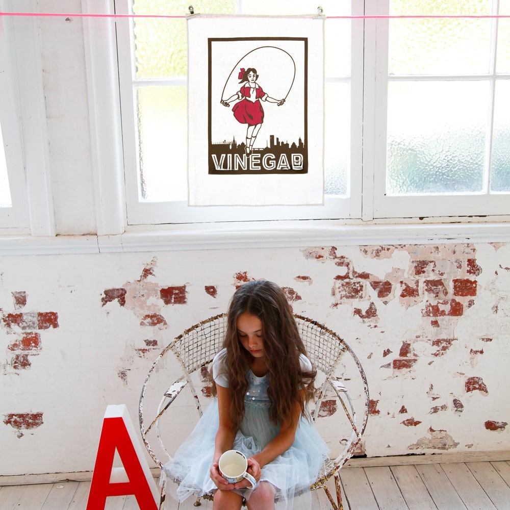 Make Me Iconic Skipping Girl tea towel featuring Melbourne’s iconic Little Audrey neon sign, a nostalgic tribute to the city’s skyline.