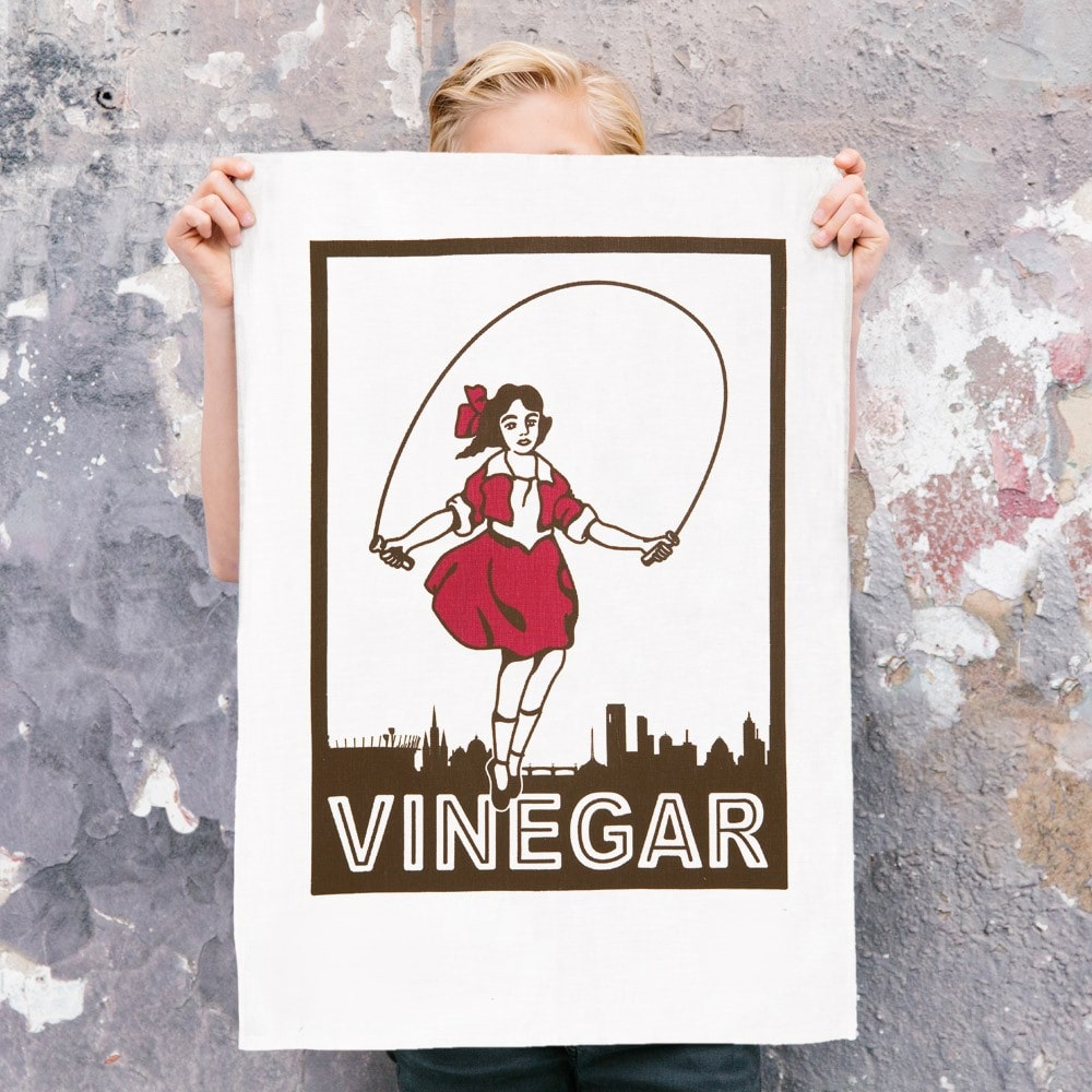 Make Me Iconic Skipping Girl tea towel featuring Melbourne’s iconic Little Audrey neon sign, a nostalgic tribute to the city’s skyline.