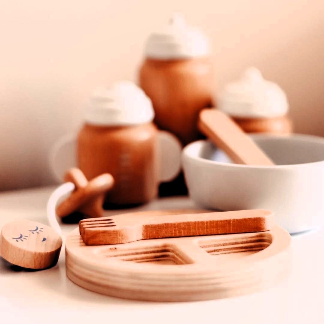 Make Me Iconic 11-piece wooden doll accessory kit with bottles, sippy cup, bowl, fork, spoon, brush with real bristles, comb, teether, and clip-on pacifier – perfect for pretend play.