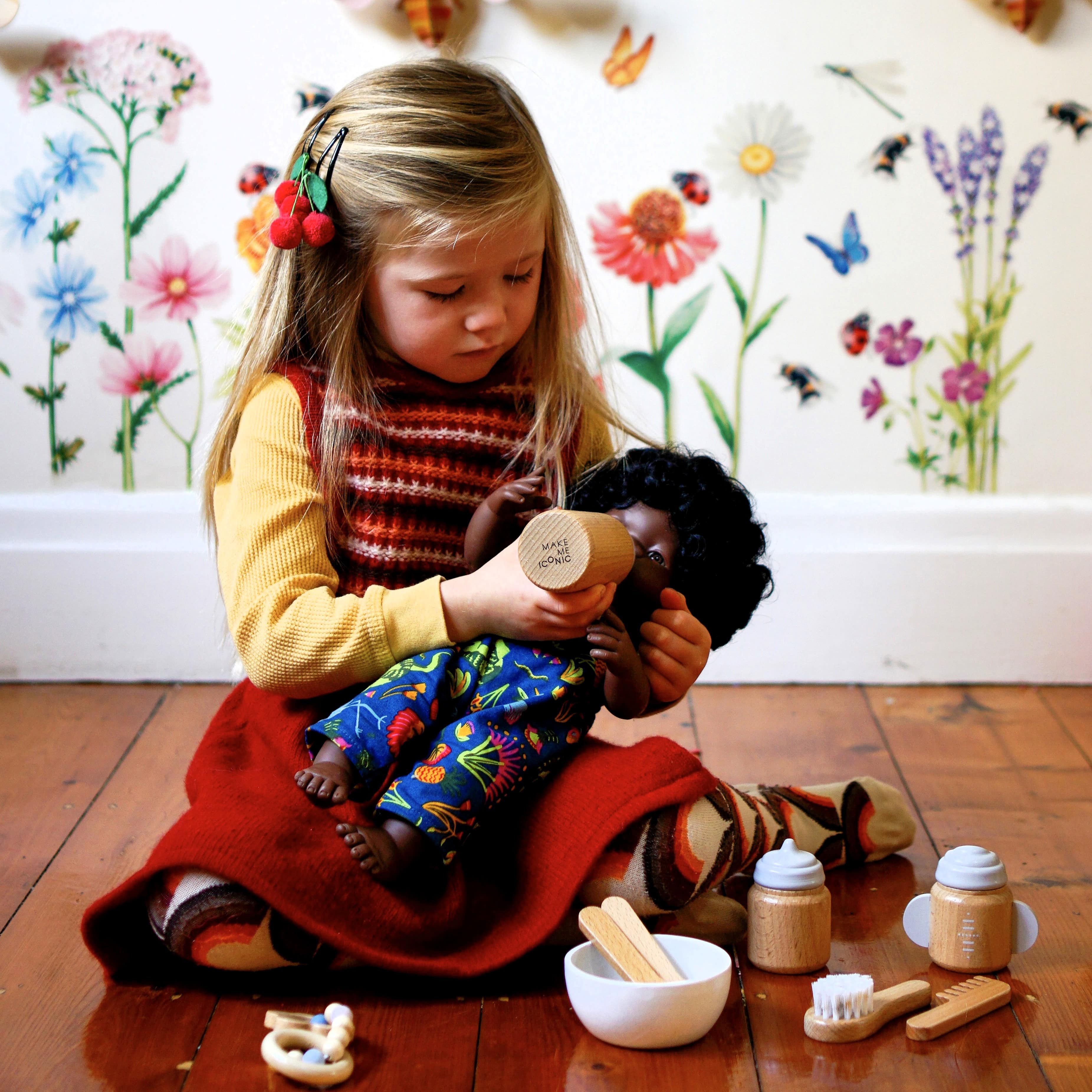 Make Me Iconic 11-piece wooden doll accessory kit with bottles, sippy cup, bowl, fork, spoon, brush with real bristles, comb, teether, and clip-on pacifier – perfect for pretend play.