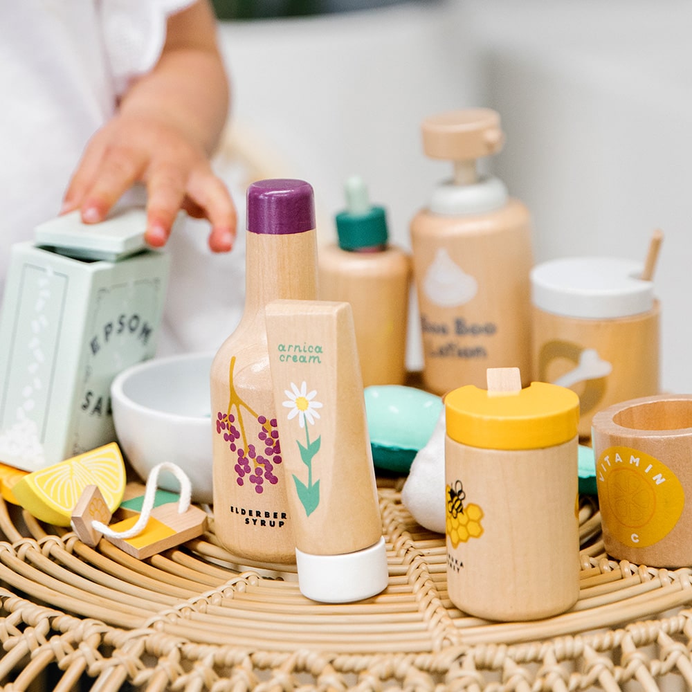 Wooden toy Natural Healers Kit with pestle and mortar, pretend Epsom salts, Manuka honey, bone broth, Tea Tree oil dropper, Boo Boo lotion, vitamins, arnica cream, herbal tea bags, and felt herbs for imaginative wellness play.
