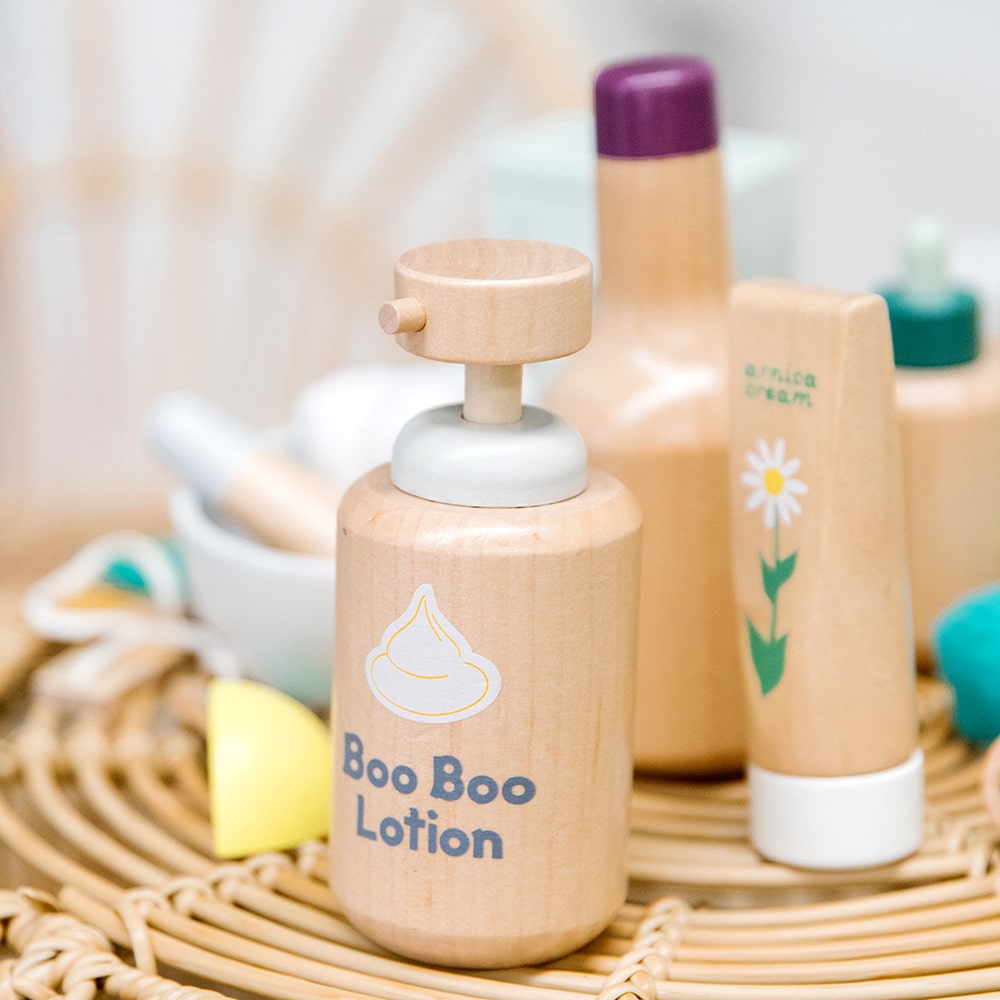 Wooden toy Natural Healers Kit with pestle and mortar, pretend Epsom salts, Manuka honey, bone broth, Tea Tree oil dropper, Boo Boo lotion, vitamins, arnica cream, herbal tea bags, and felt herbs for imaginative wellness play.