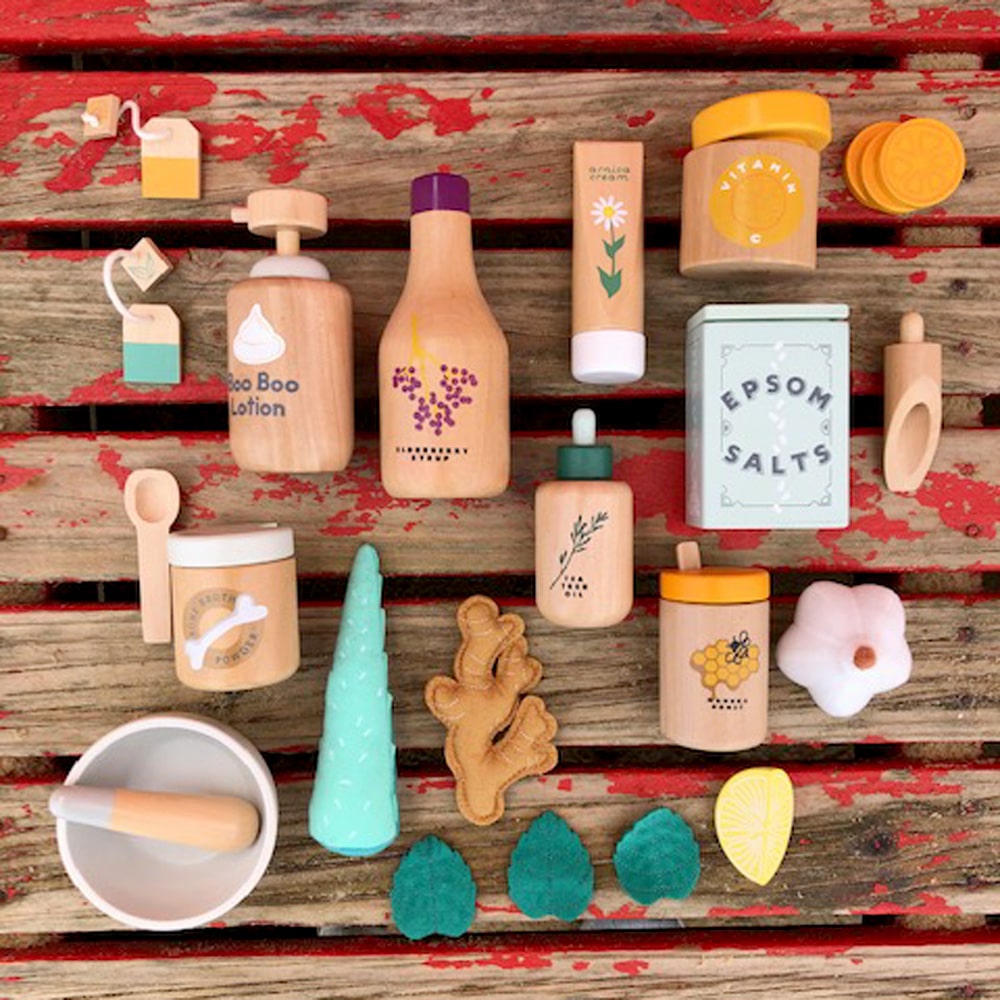 Wooden toy Natural Healers Kit with pestle and mortar, pretend Epsom salts, Manuka honey, bone broth, Tea Tree oil dropper, Boo Boo lotion, vitamins, arnica cream, herbal tea bags, and felt herbs for imaginative wellness play.