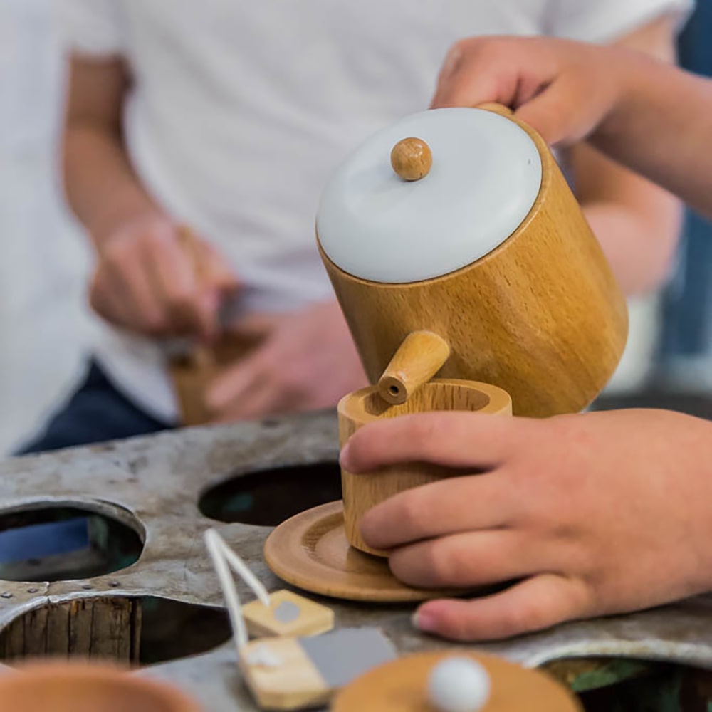 Wooden toy tea set for kids featuring teapot, cups, saucers, spoons, sugar bowl and milk jug, designed for pretend play, café role-play, and social learning activities.