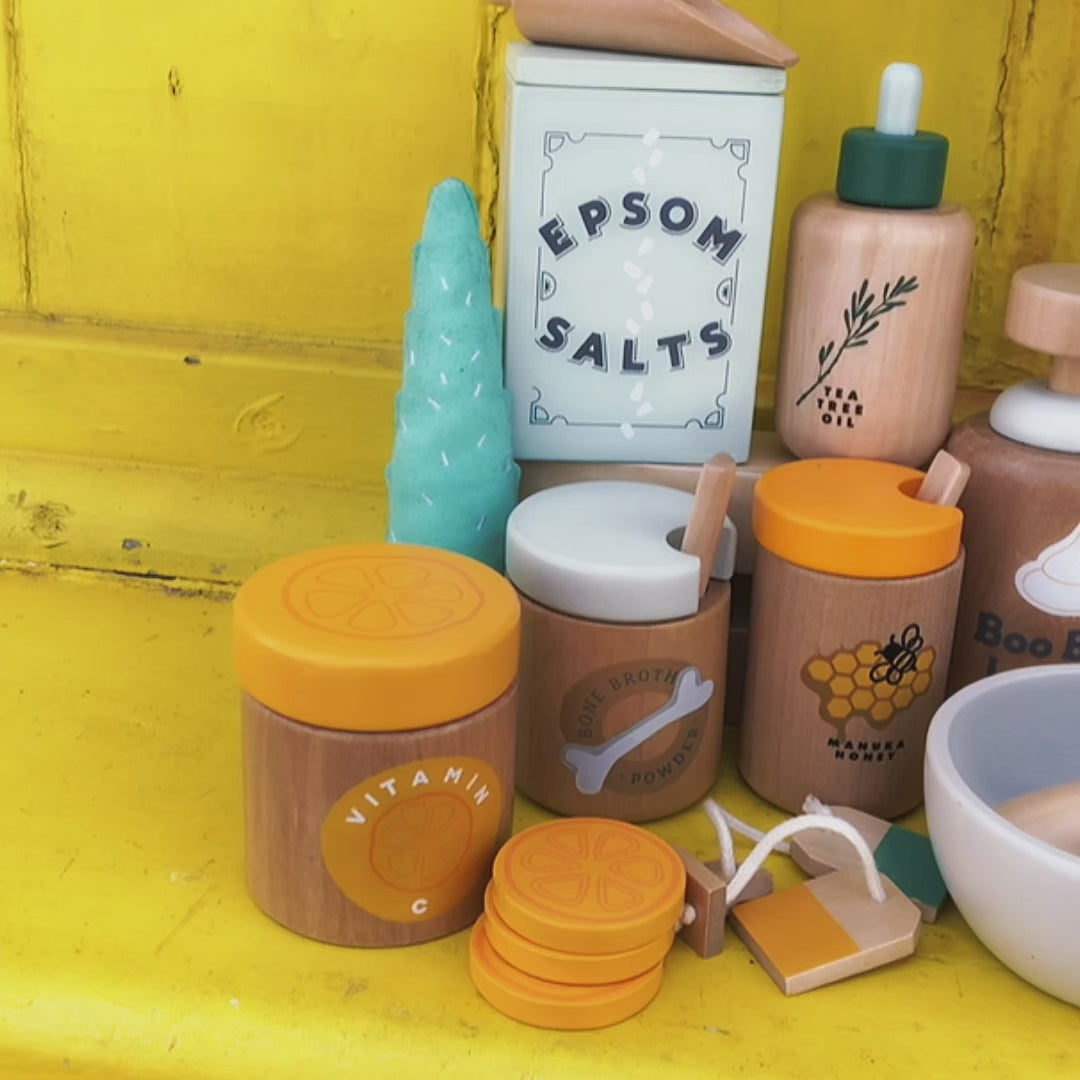 Make Me Iconic wooden toy Natural Healers Kit with pestle and mortar, pretend Epsom salts, Manuka honey, bone broth, Tea Tree oil dropper, Boo Boo lotion, vitamins, arnica cream, herbal tea bags, and felt herbs for imaginative wellness play.