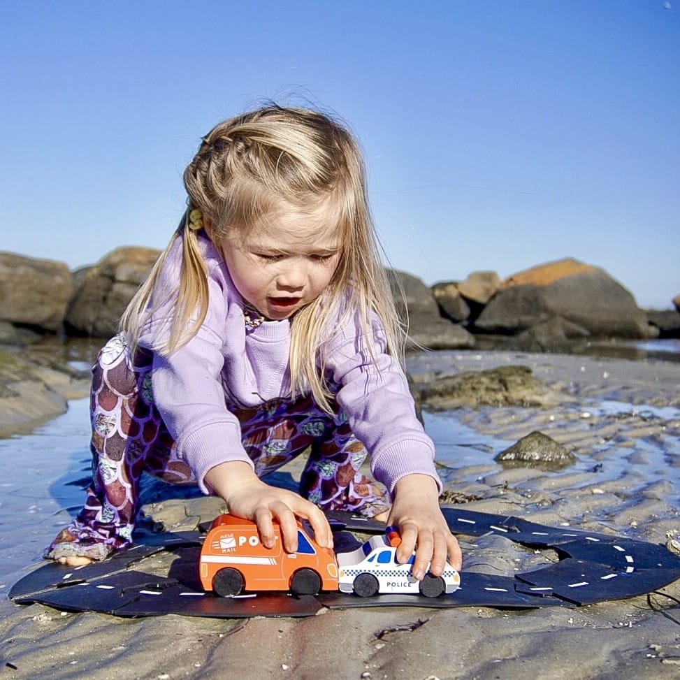 Child playing with wooden Aussie toy cars on the beach, enjoying outdoor imaginative play with eco-friendly wooden vehicles. Bring imaginative outdoor play to life with iconic wooden Aussie vehicles