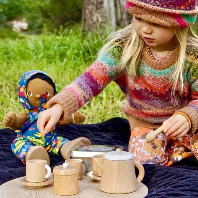 Child playing with a wooden tea set outdoors with dolls and teddy bears during a pretend tea party, encouraging imaginative open-ended play
