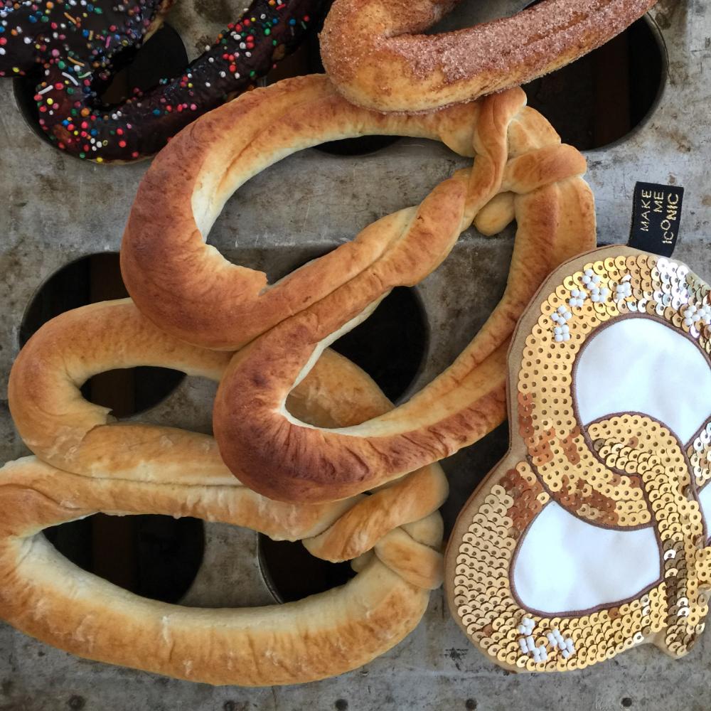 Make Me Iconic sequin pretzel purse with sparkling gold and pink sequins shaped like a pretzel, designed for holding small essentials like coins, keys, or hair clips. A fun, eye-catching accessory for kids, teens, and anyone who loves a playful touch of glamour.