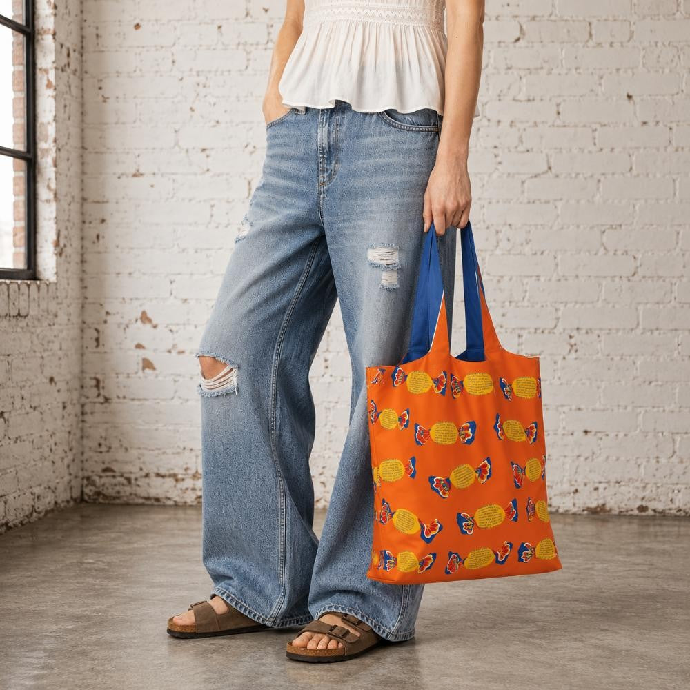 A Make Me Iconic reusable foldable shopping bag featuring a nostalgic Fantale lolly design on a vibrant orange background. Made from 100% recycled fabric, this lightweight bag folds into its own matching pouch, making it perfect for shopping, travel, or everyday use while celebrating one of Australia's most iconic treats.