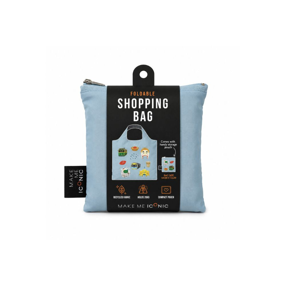 A Make Me Iconic reusable foldable shopping bag featuring iconic Melbourne landmarks and symbols including a W-Class tram, MCG, Flinders Street Station, coffee, meat pie, rain, and AFL football. Made from 100% recycled fabric, this lightweight eco-friendly tote folds into a compact pouch for shopping, travel, and everyday use.