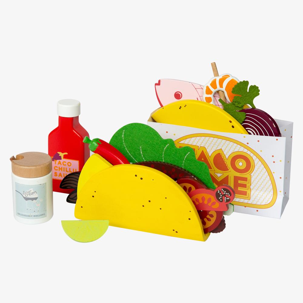 Make Me Iconic 21-piece wooden toy play Taco Kit featuring stand-up taco shells, prawns on skewers, paper takeaway bags, felt toppings, and pretend condiments like chilli sauce and sour cream for imaginative role play.