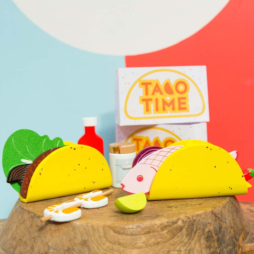 Make Me Iconic 21-piece wooden toy play Taco Kit featuring stand-up taco shells, prawns on skewers, paper takeaway bags, felt toppings, and pretend condiments like chilli sauce and sour cream for imaginative role play.