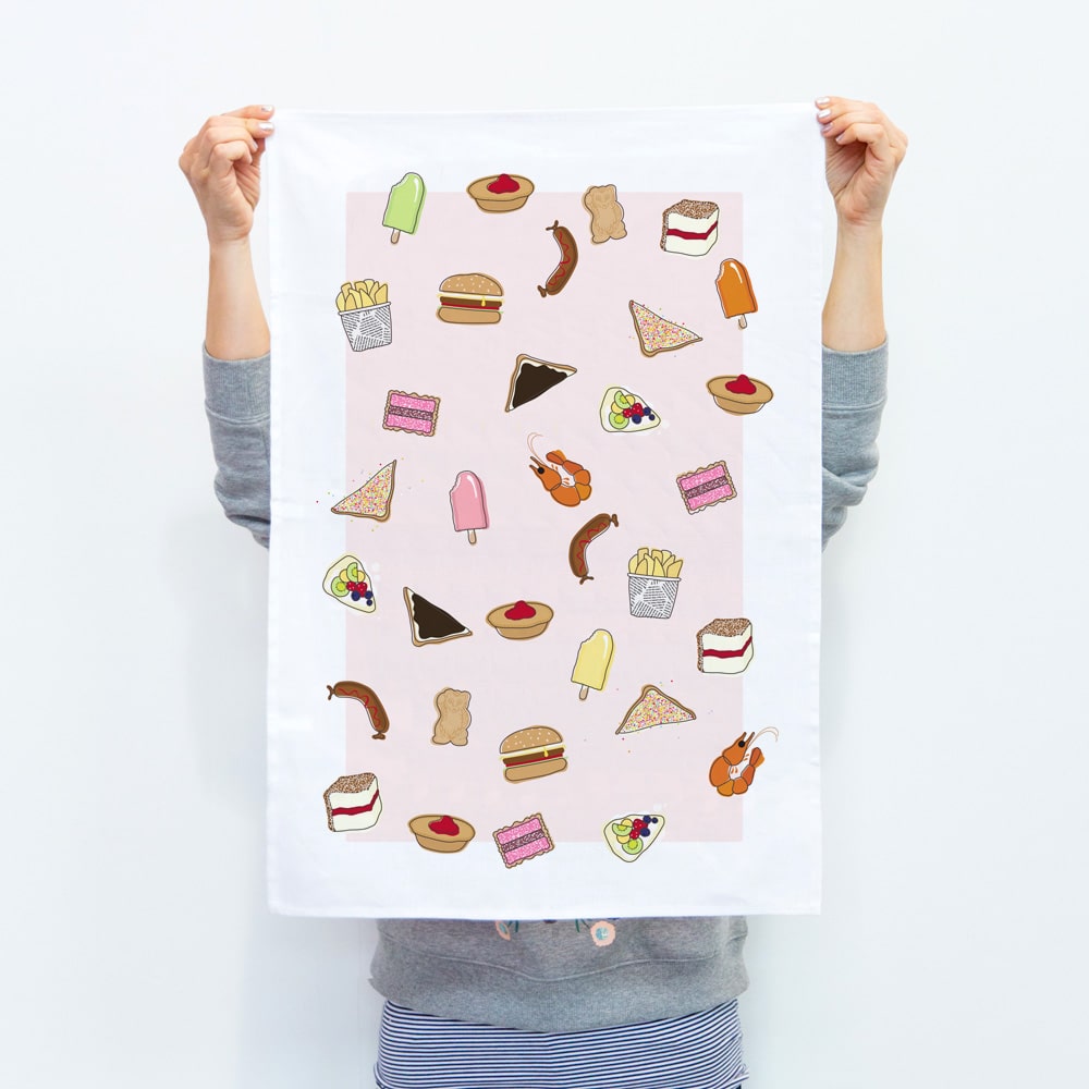 Make Me Iconic tea towel featuring iconic Australian foods like Vegemite toast, fairy bread, meat pie, pavlova, and lamingtons. A colourful, quirky kitchen accessory celebrating Aussie culture and nostalgia