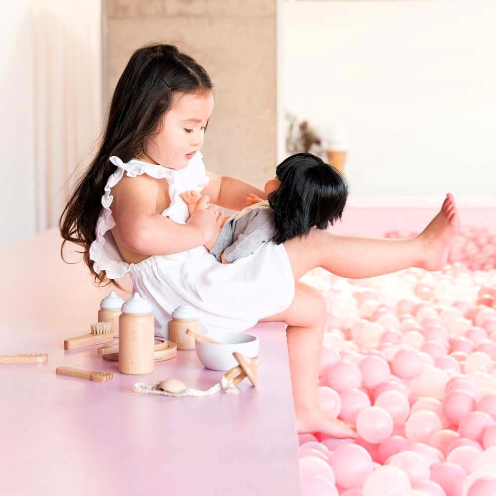 Make Me Iconic 11-piece wooden toy doll accessory kit with bottles, sippy cup, bowl, fork, spoon, brush with real bristles, comb, teether, and clip-on pacifier, perfect for pretend play.