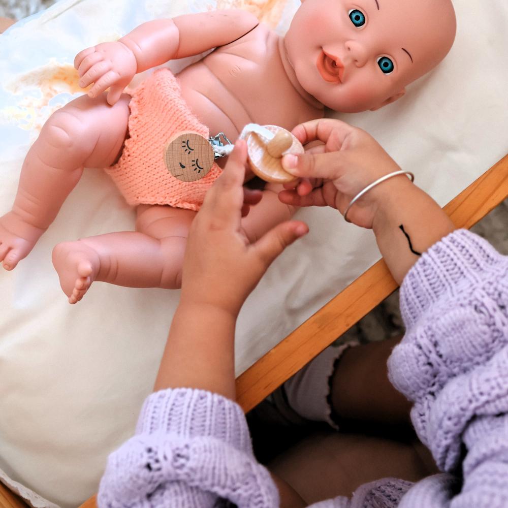 Make Me Iconic 11-piece wooden toy doll accessory kit with bottles, sippy cup, bowl, fork, spoon, brush with real bristles, comb, teether, and clip-on pacifier, perfect for pretend play.