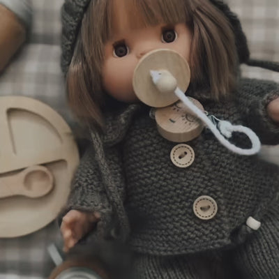 Make Me Iconic 11-piece wooden doll accessory kit with bottles, sippy cup, bowl, utensils, brush with real bristles, and clip-on pacifier for pretend play.