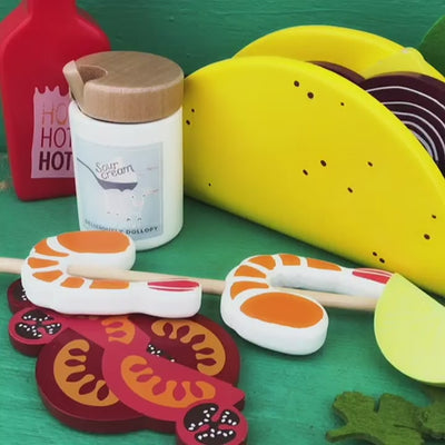 Make Me Iconic 21-piece wooden toy play Taco Kit featuring stand-up taco shells, prawns on skewers, paper takeaway bags, felt toppings, and pretend condiments like chilli sauce and sour cream for imaginative role play.